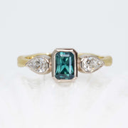 Ring with teal sapphire and pear-shaped diamonds on a white background