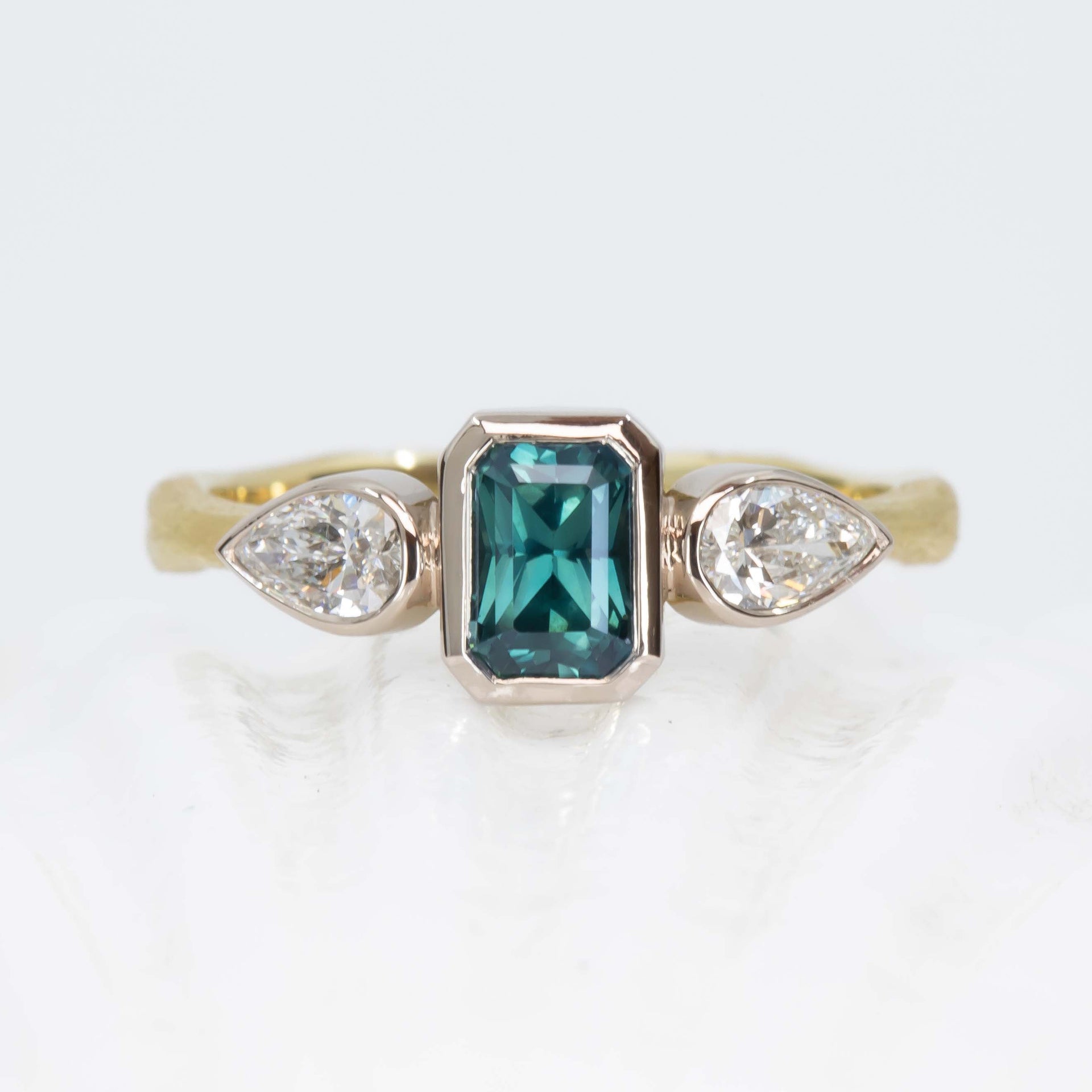 Ring with teal sapphire and pear-shaped diamonds on a white background