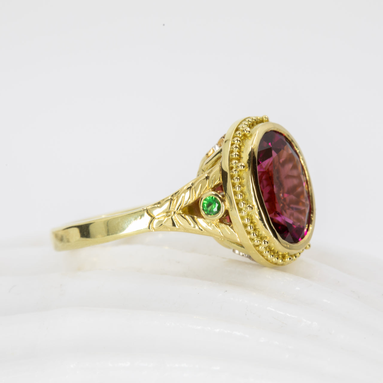 Gold ring with a large red gemstone and smaller green gemstone on a white background