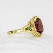 Gold ring with a large red gemstone and smaller green gemstone on a white background