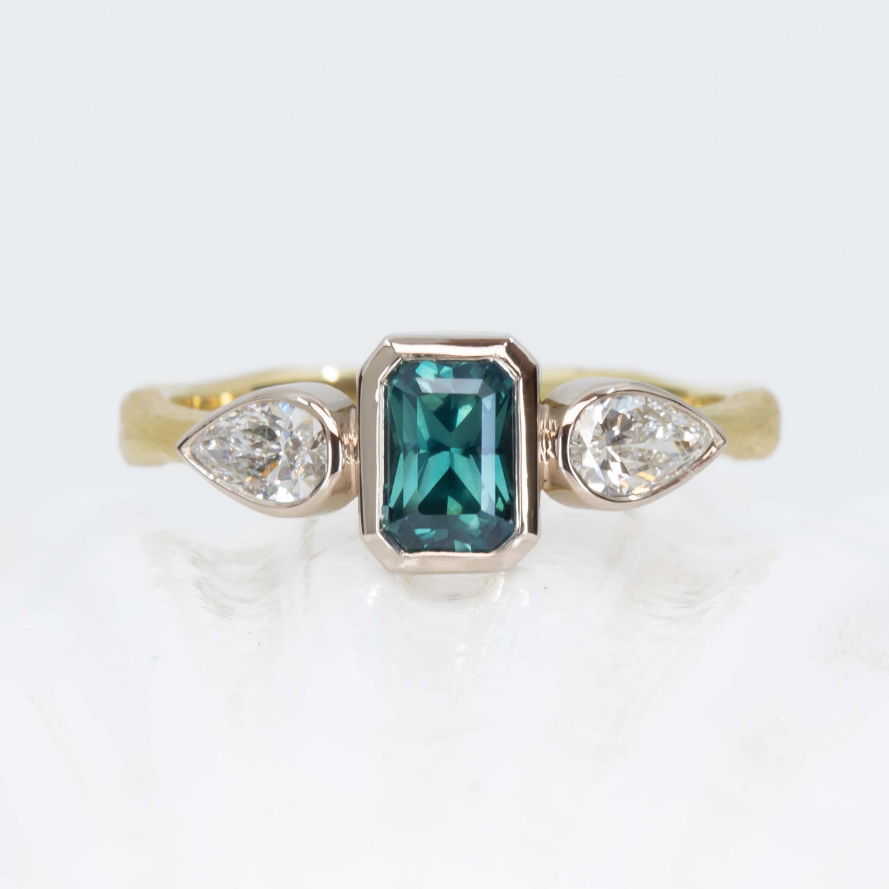 Ring with teal sapphire and pear-shaped diamonds on a white background